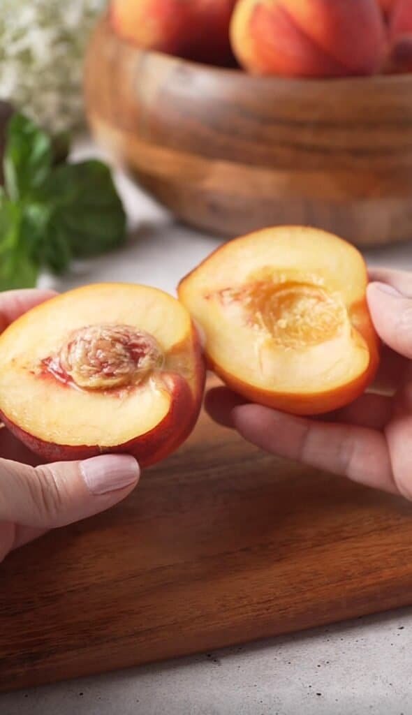 Hands holding two peach halves with pit removed, prepping peaches for burrata salad