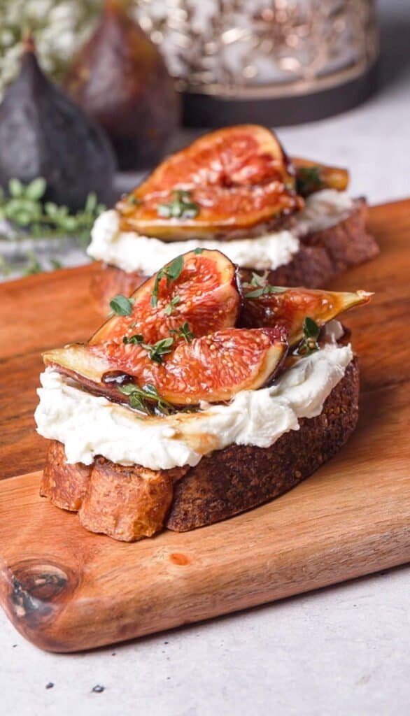 Marinated fig and goat cheese crostini topped with fresh thyme on a wood board