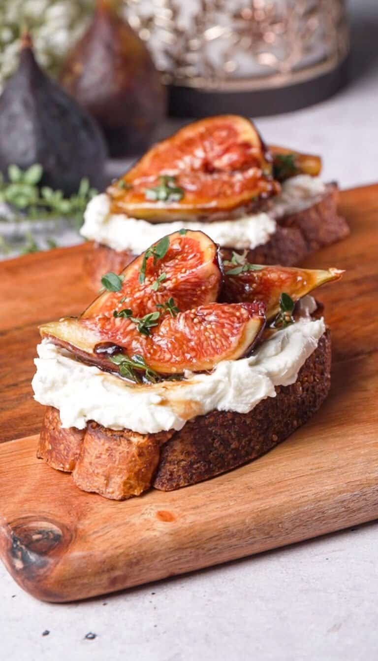 Marinated fig and goat cheese crostini topped with fresh thyme on a wood board