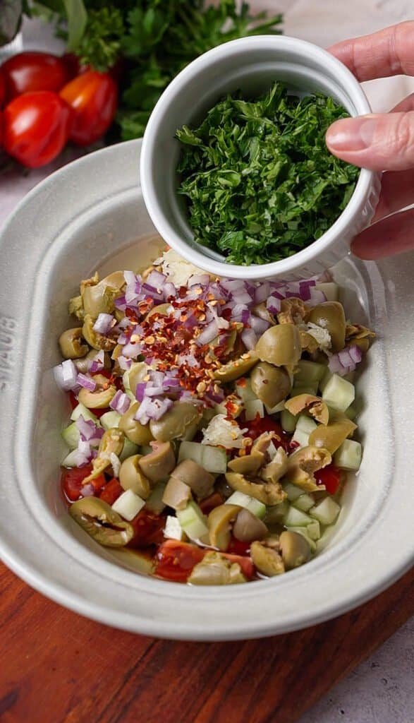Fresh chopped parsley being added to Mediterranean tomato dip with red onion and red pepper flakes