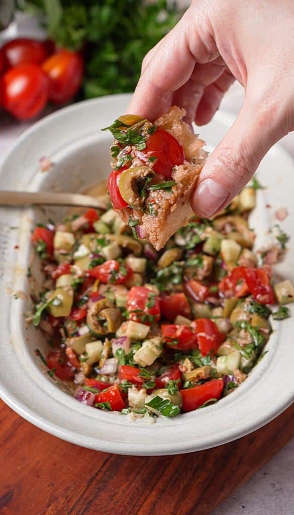 Piece of bread scooping up Mediterranean tomato dip with olives and fresh herbs