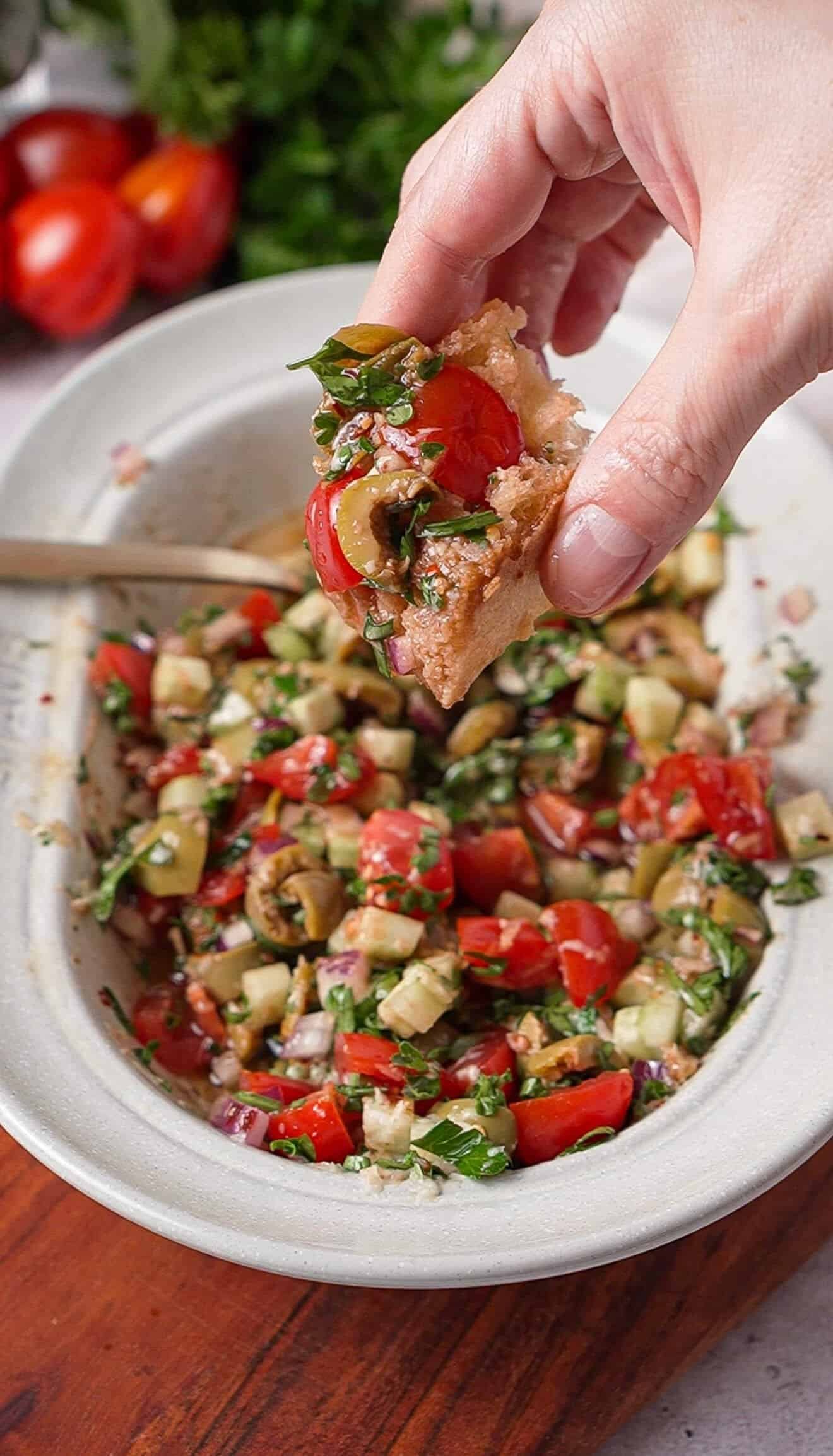 Piece of bread scooping up Mediterranean tomato dip with olives and fresh herbs