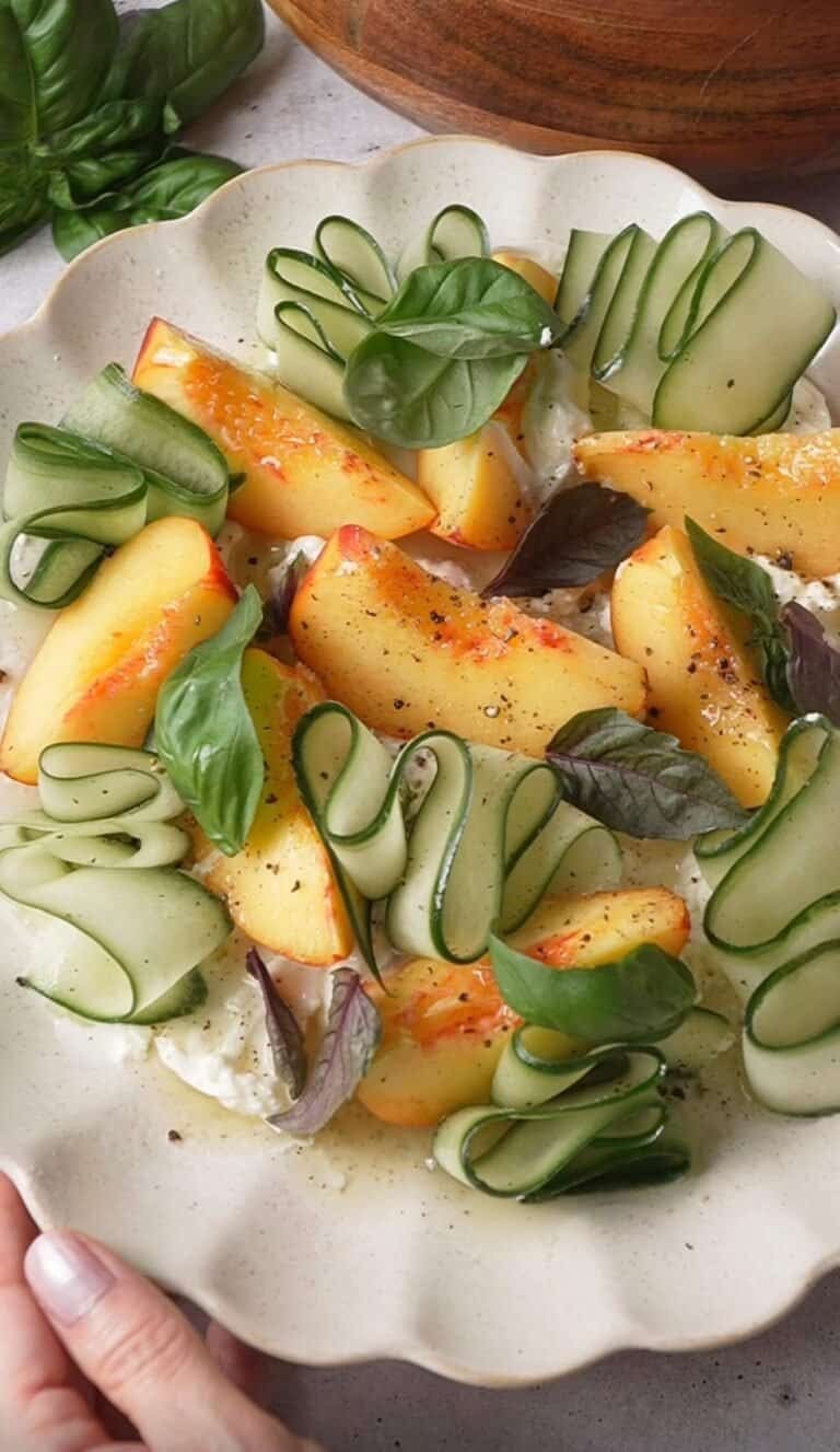 Close-up of peach burrata salad with torn burrata, cucumber ribbons, and purple and green basil leaves
