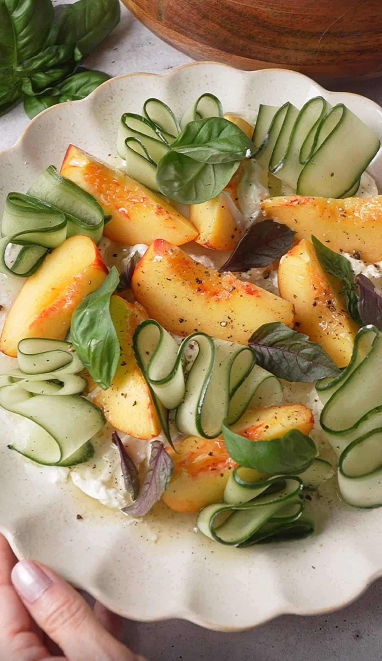 Close-up of peach burrata salad with torn burrata, cucumber ribbons, and purple and green basil leaves