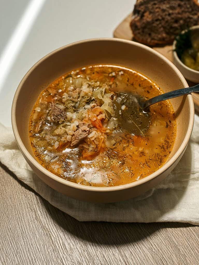 Close-up of rassolnik pickle soup with beef and barley, spoon resting in bowl