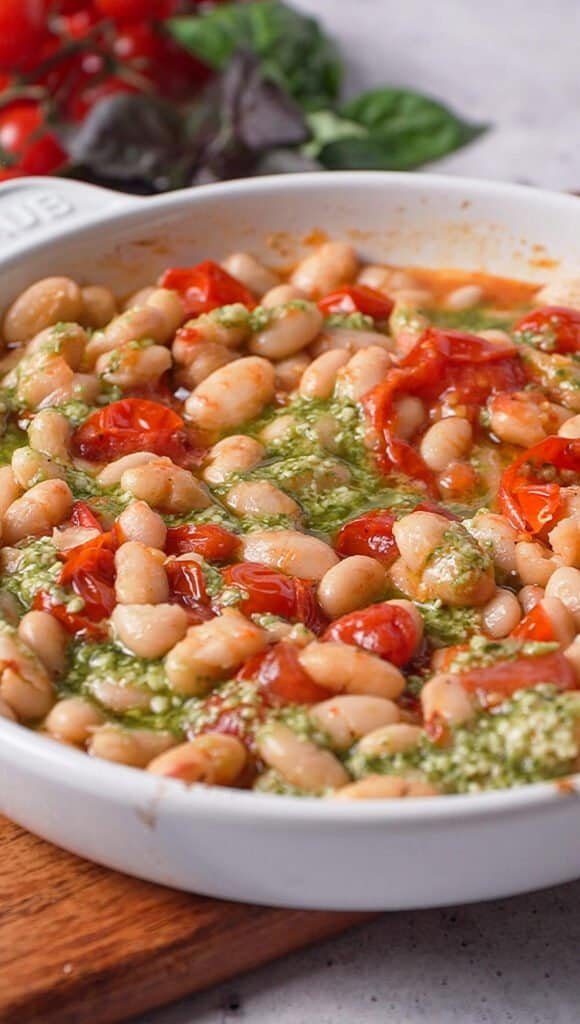 Close-up of roasted white beans and tomatoes swirled with basil pesto before adding burrata