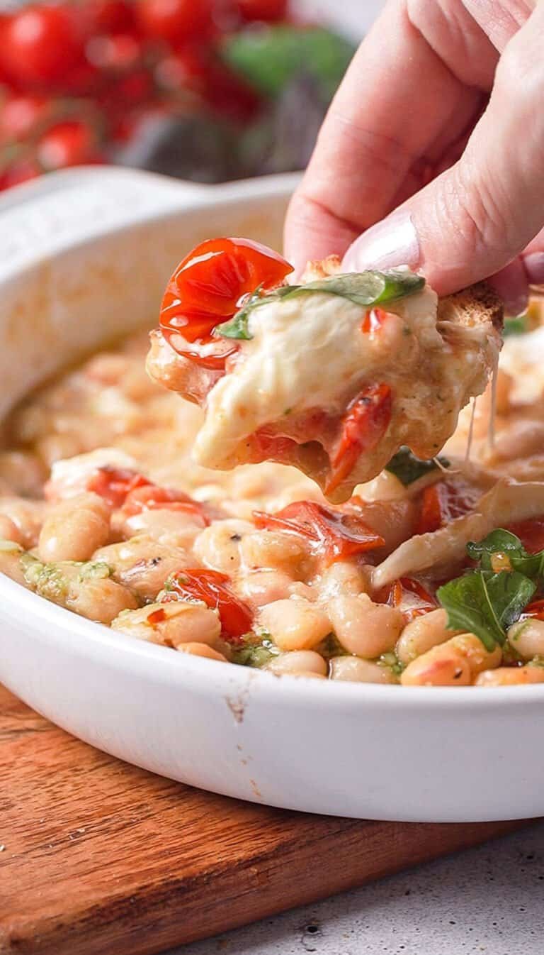Hand dipping toasted bread into roasted tomato white bean dip with melted burrata and a cheese pull