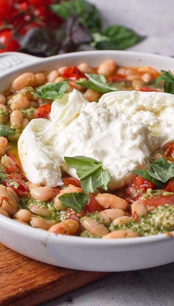 Whole ball of burrata nestled into roasted tomatoes and white beans in a Staub baking dish
