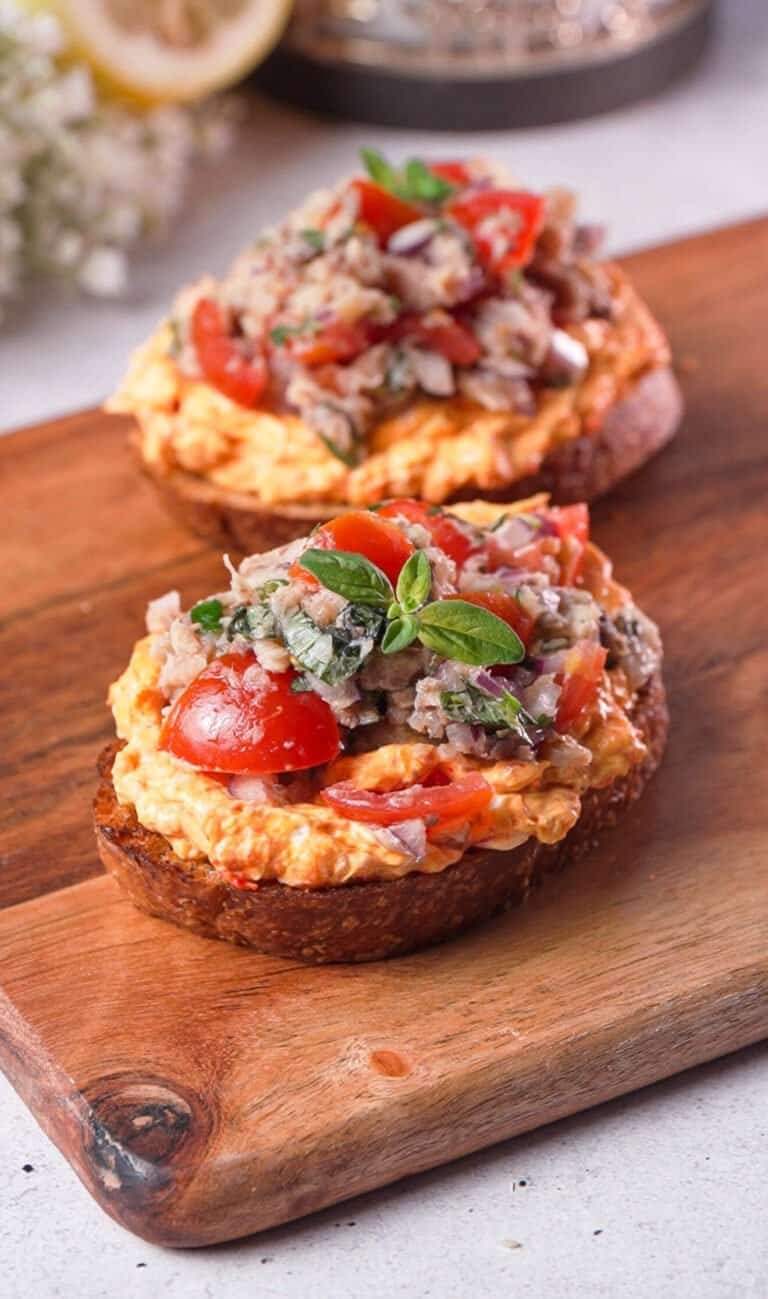 Two sardine toasts with harissa cream cheese and fresh tomatoes on a wood board