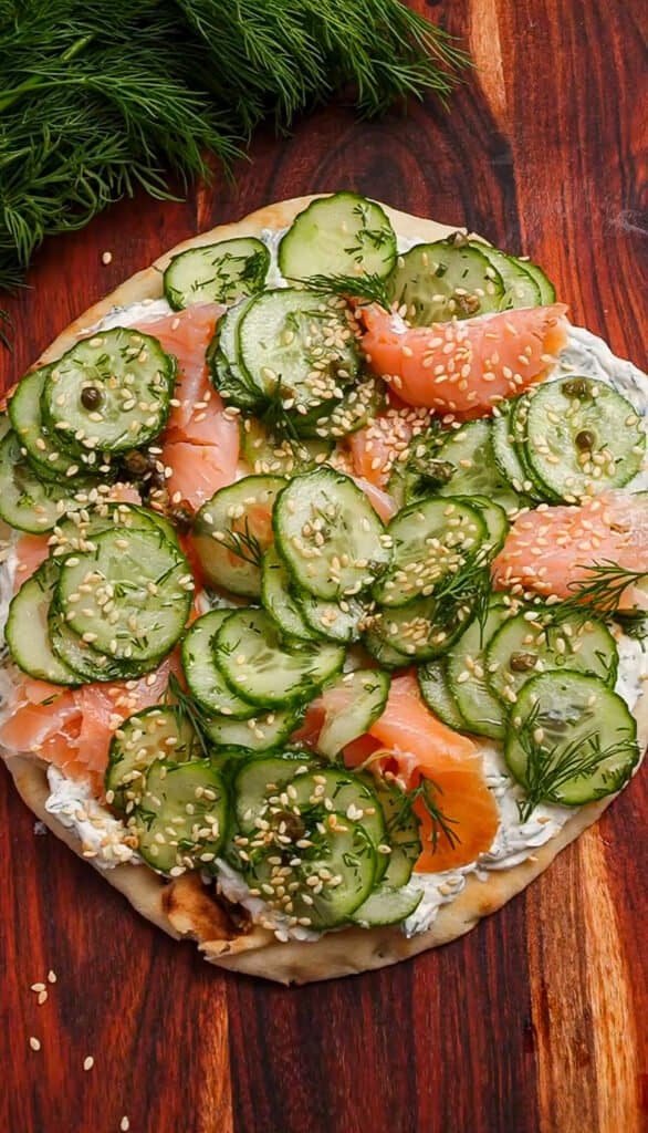 Close-up of cucumber and salmon pizza with sesame seeds on wooden table.