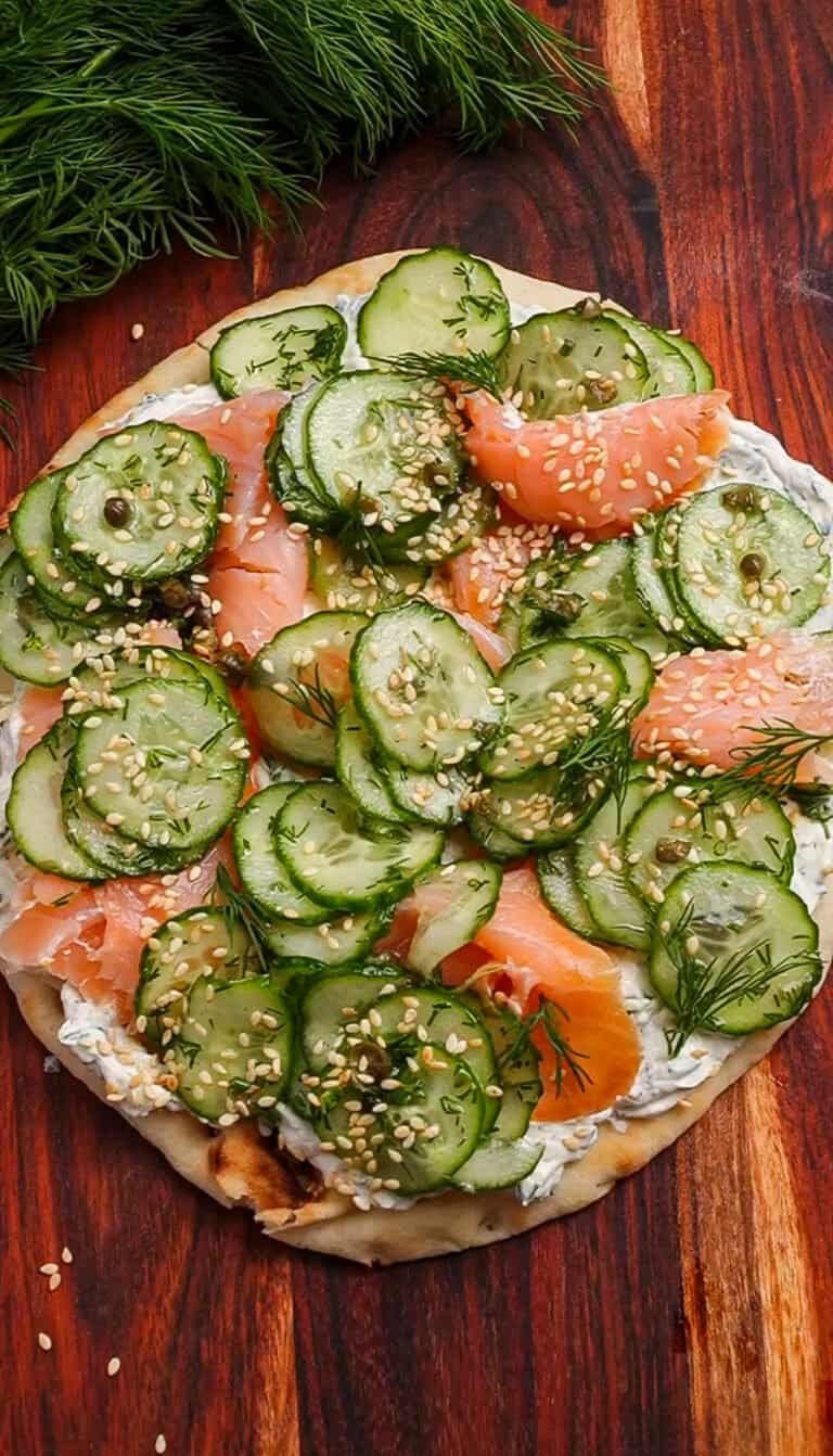 Close-up of cucumber and salmon pizza with sesame seeds on wooden table.