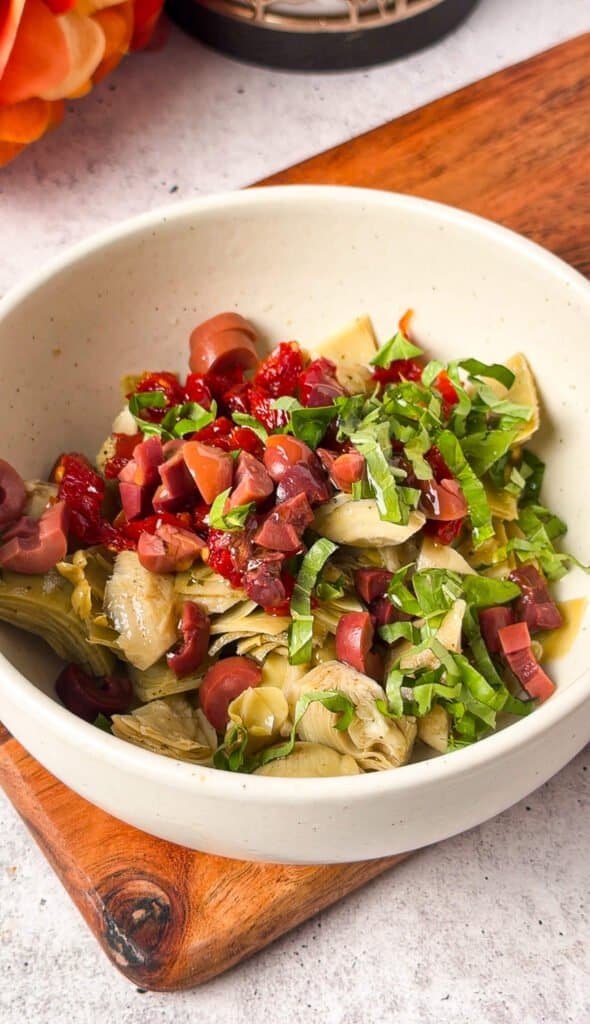 Marinated artichoke, sun-dried tomato, and Kalamata olive topping tossed in a bowl with fresh basil