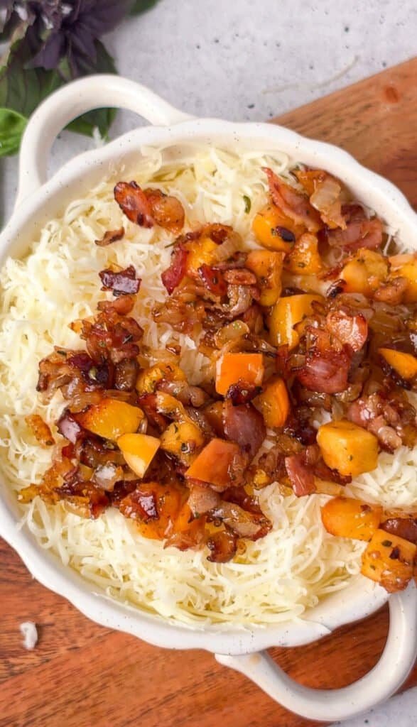 Shredded cheese topped with caramelized bacon, onion, and peach before baking
