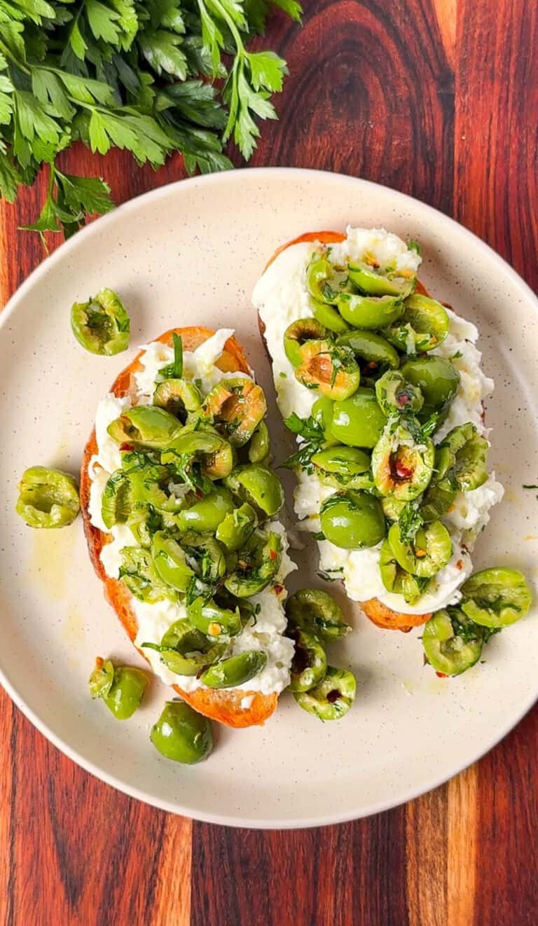 Two burrata toasts topped with torn marinated Castelvetrano olives on a plate