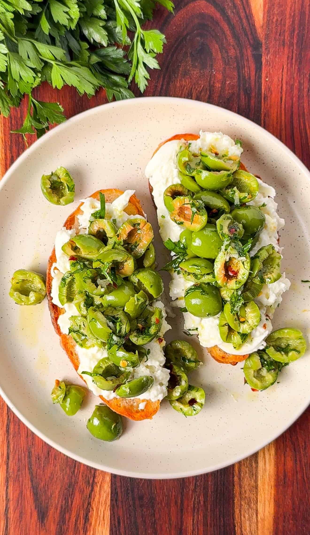 Two burrata toasts topped with torn marinated Castelvetrano olives on a plate