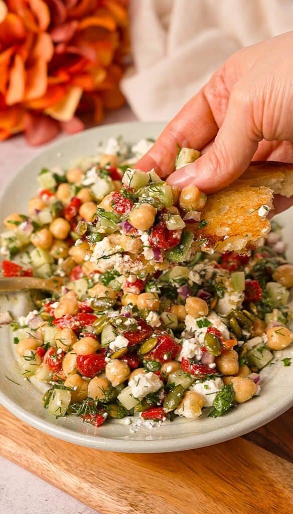 toasted bread scooping up chickpea salad with feta, roasted red pepper, and dill