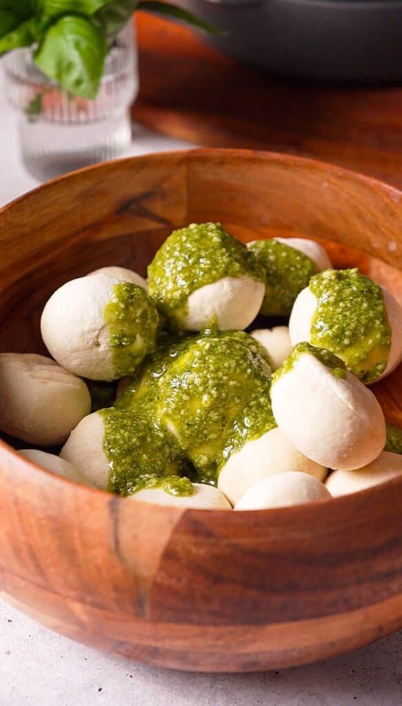 frozen dinner roll dough balls being tossed with basil pesto in a wooden bowl