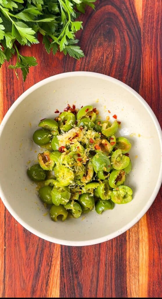 Torn Castelvetrano olives in a bowl with lemon zest, garlic, and red pepper flakes