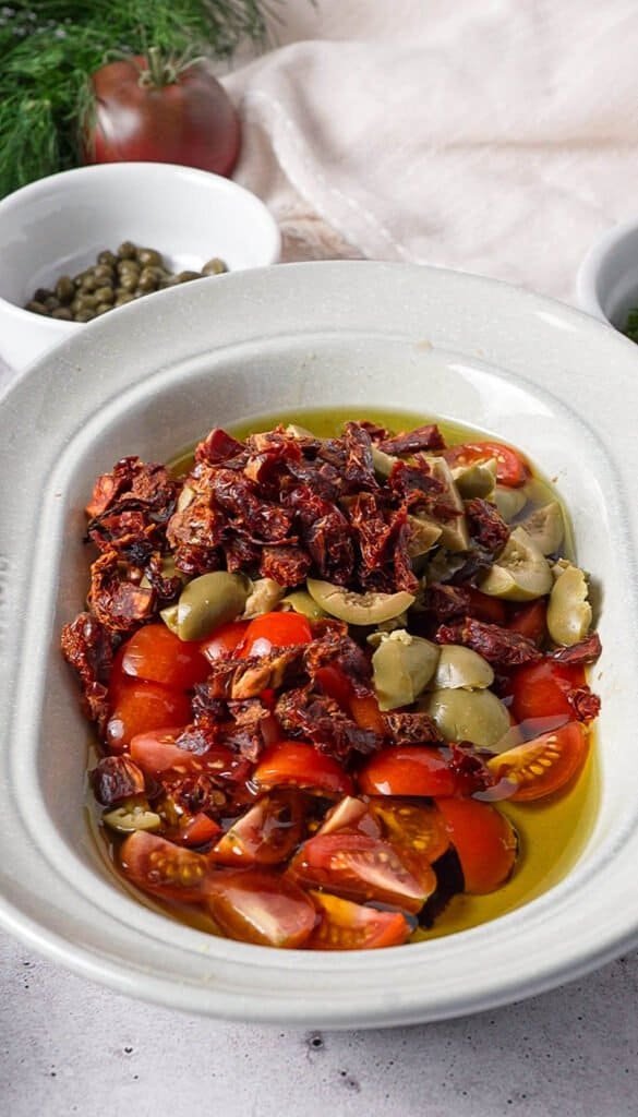 Sun-dried tomatoes, green olives, and cherry tomatoes in a bowl before mixing