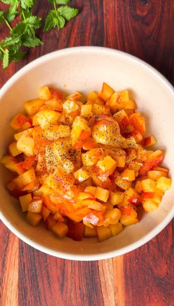 Diced peaches tossed with olive oil and black pepper in a bowl for peach goat cheese appetizer