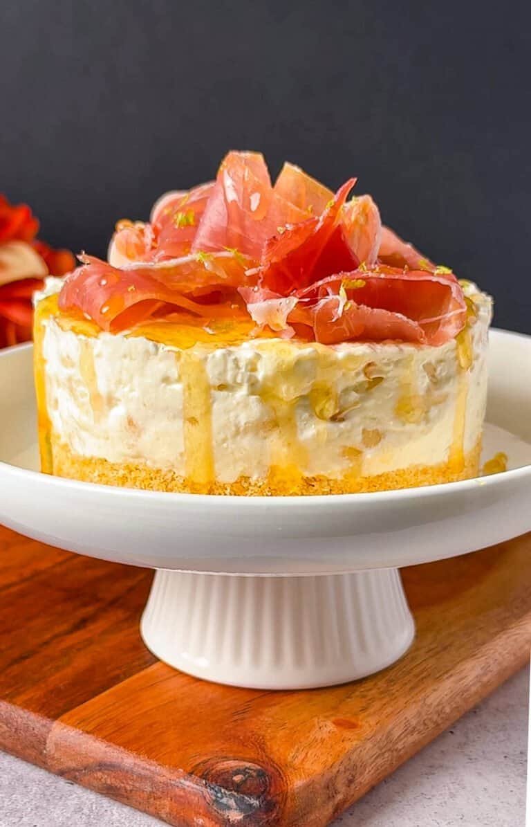 Pear cheesecake appetizer on a cake stand topped with prosciutto ribbons and honey