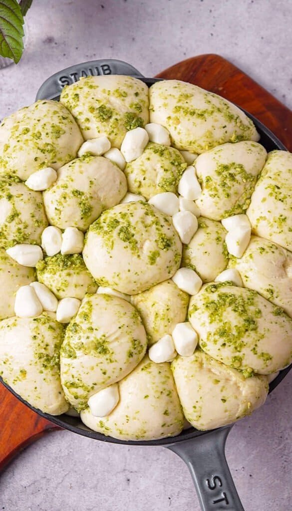 pesto covered dinner roll dough balls layered with mozzarella pearls in a cast iron skillet
