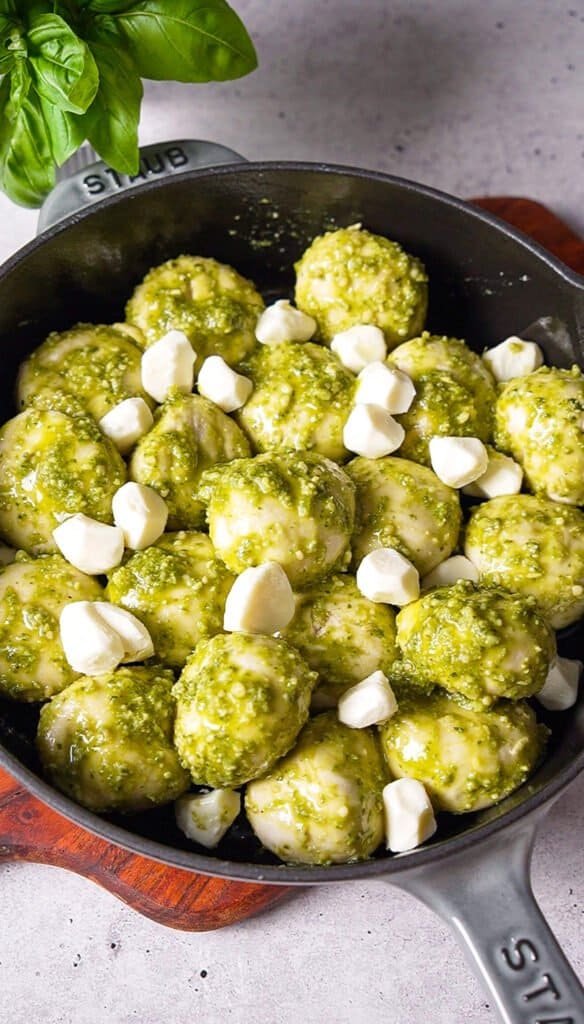 pesto coated dough balls and mozzarella pearls arranged in a skillet before baking