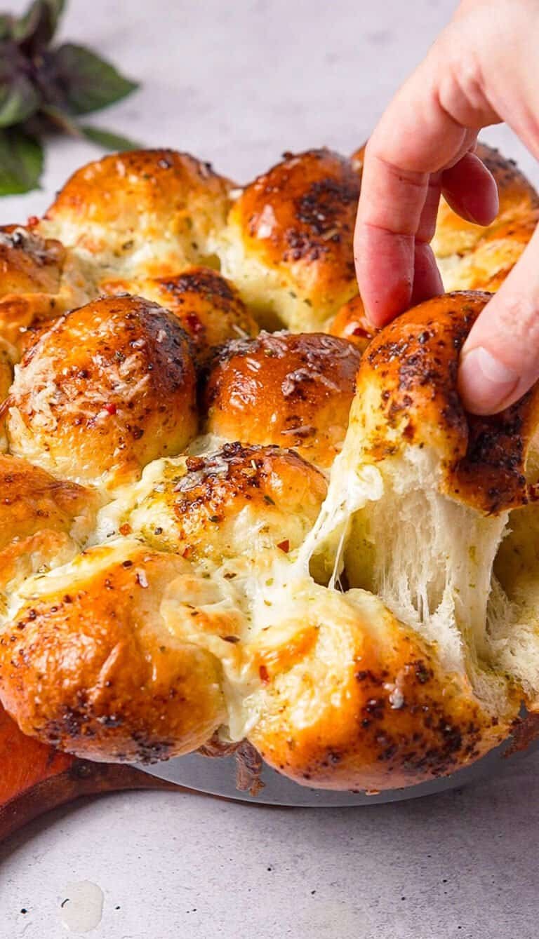 hand pulling a cheesy piece from baked pesto pull apart bread with mozzarella stretching