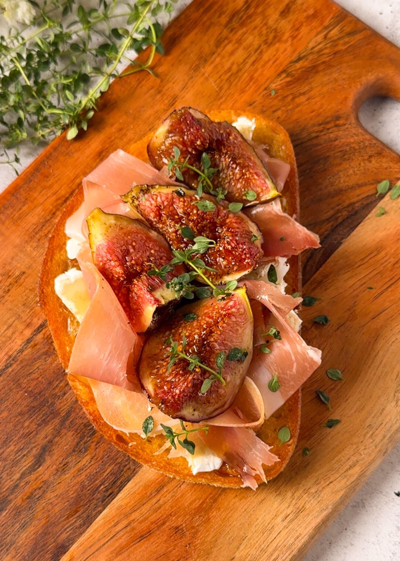 Overhead view of roasted fig and brie toast with prosciutto and thyme on a wooden board