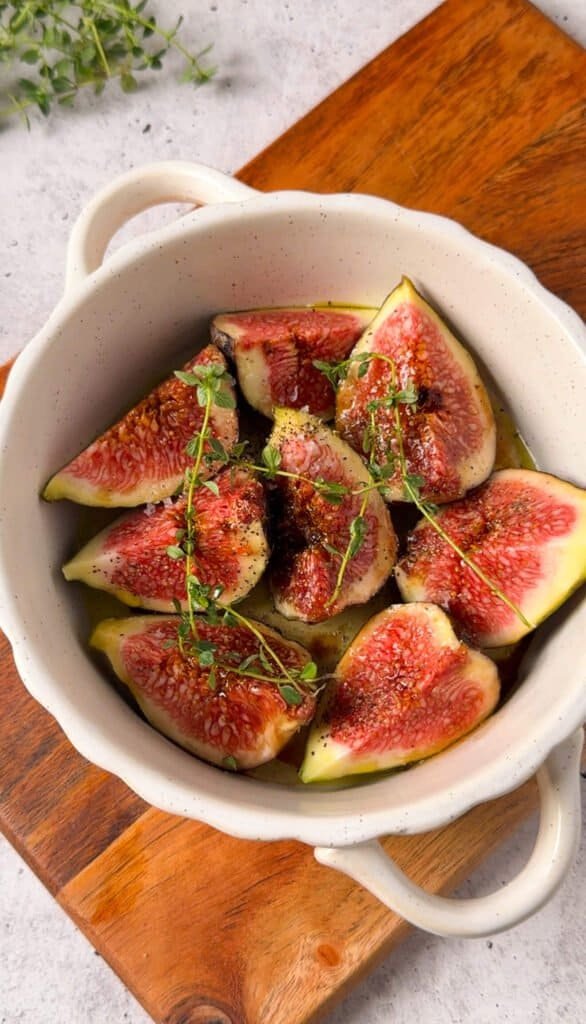 Fig quarters roasting in a small dish with honey, balsamic and fresh thyme sprigs