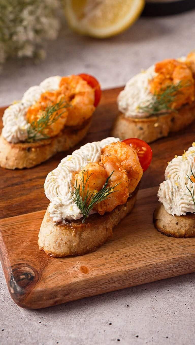 Whipped crab and garlic shrimp crostini topped with cherry tomato and dill on a wood board