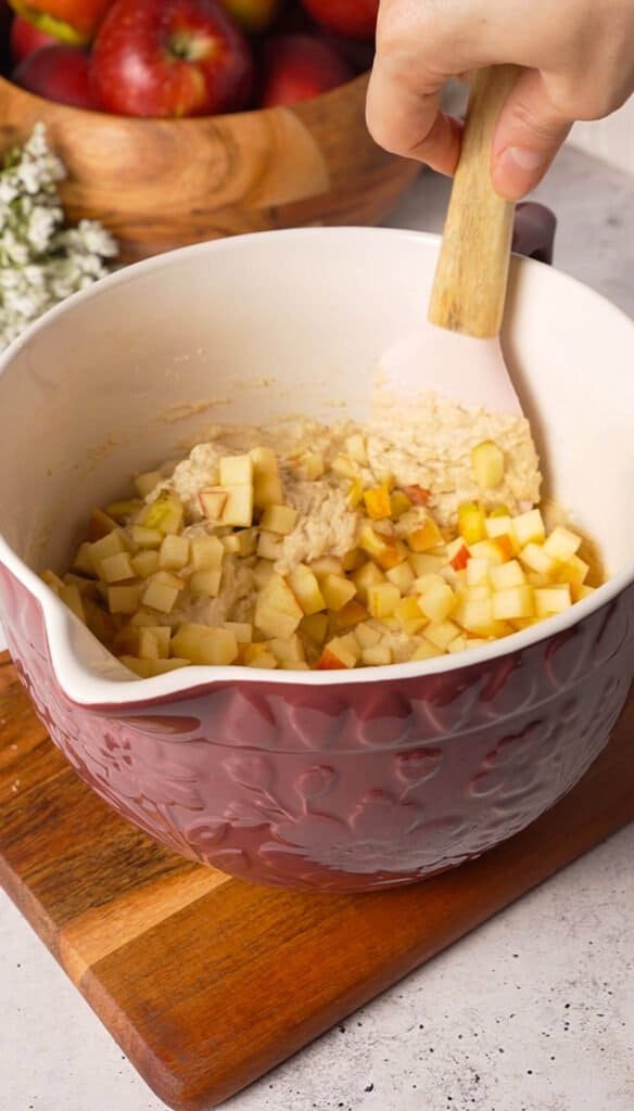 Folding diced apple into spiced cupcake batter in a mixing bowl