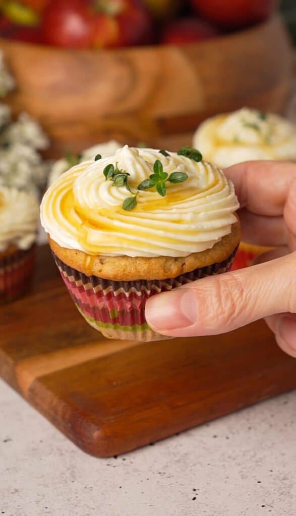 Hand holding a single apple cupcake topped with brie frosting and honey