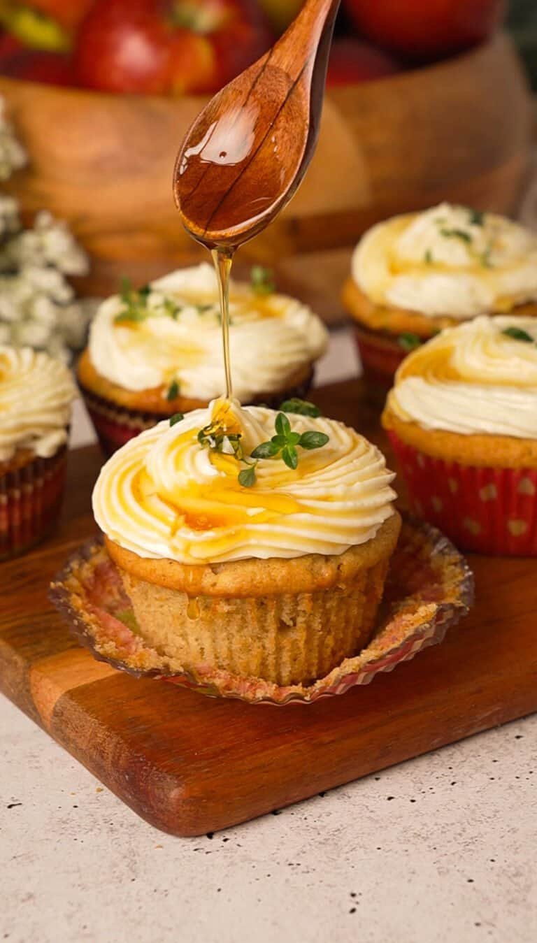 Honey drizzling over a frosted apple cupcake from a wooden spoon