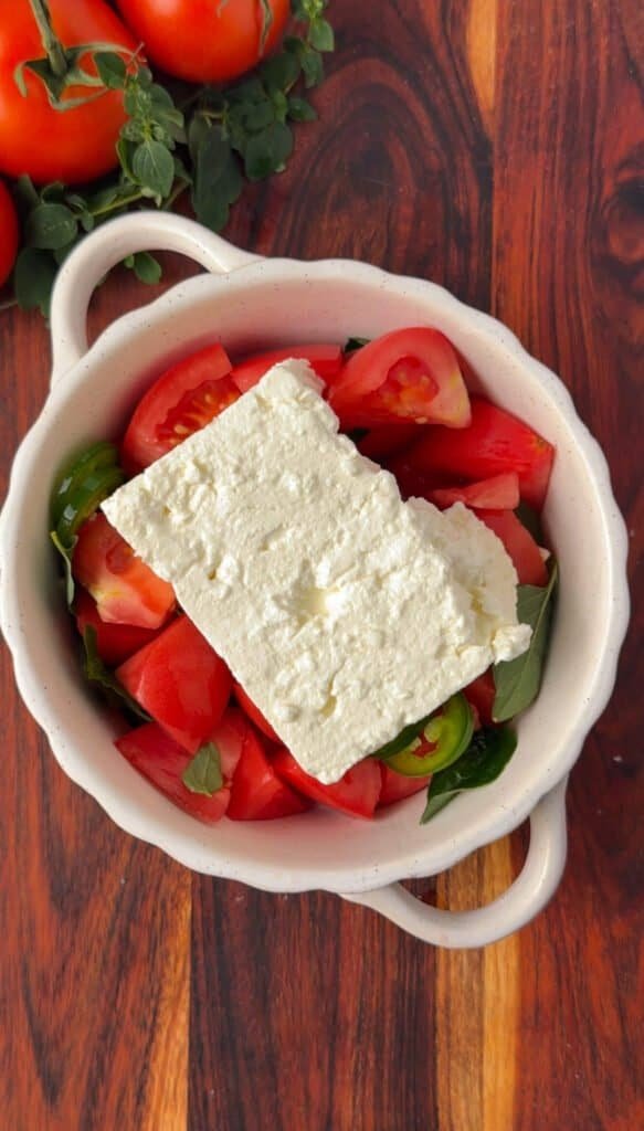 Block of feta cheese nestled into tomatoes and peppers in a baking dish