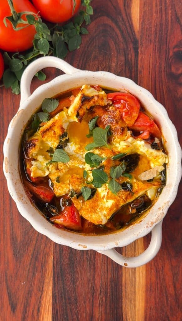 Overhead shot of rustic baked feta with tomatoes and peppers, garnished with fresh oregano