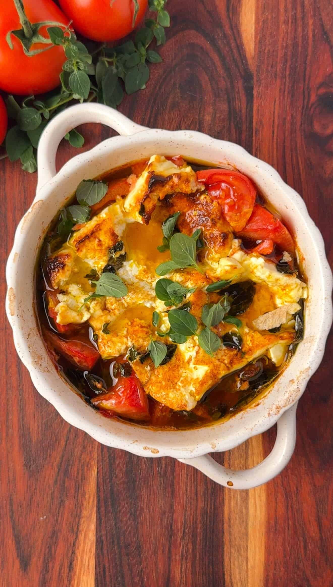 Overhead shot of rustic baked feta with tomatoes and peppers, garnished with fresh oregano