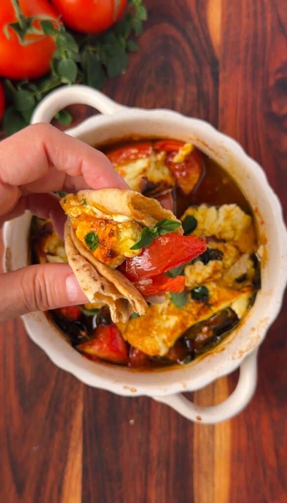 Pita bread scooping up warm baked feta with tomatoes and peppers