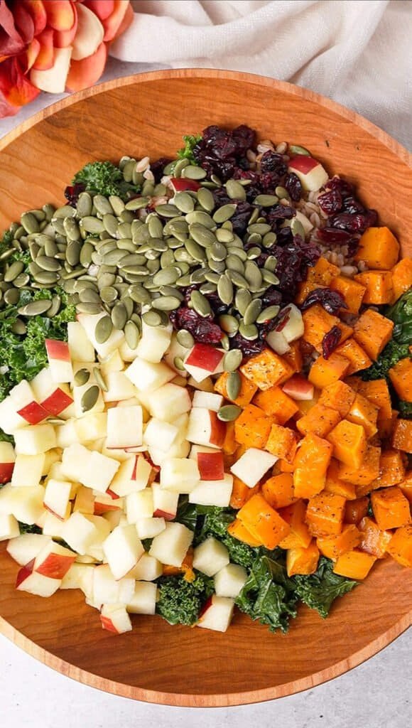 Kale farro salad ingredients arranged in sections, including massaged kale, farro, roasted squash, diced apple, dried cranberries, and toasted pepitas