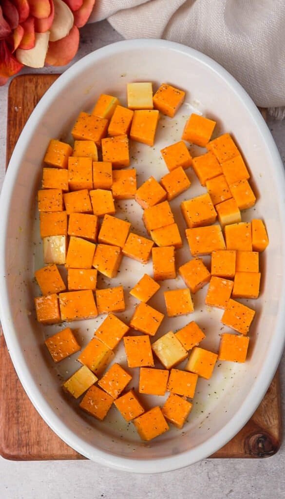 Cubed butternut squash seasoned with salt and pepper in a white baking dish before roasting
