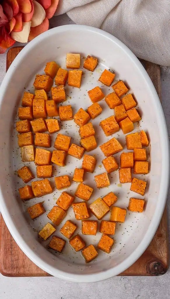 Roasted butternut squash cubes caramelized at the edges in a white baking dish