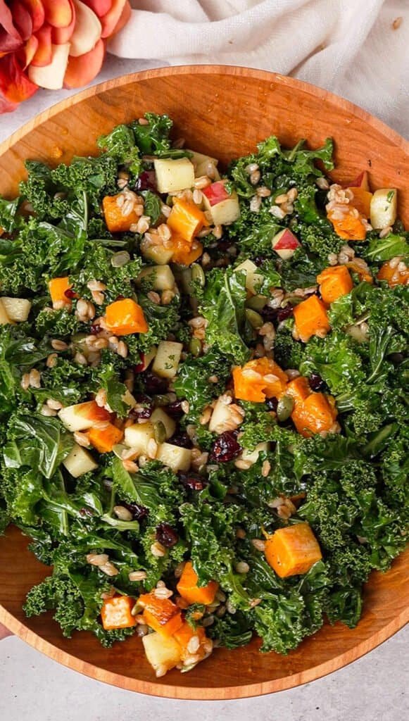 Kale farro salad tossed with roasted butternut squash, apple, and cranberries in a wooden bowl