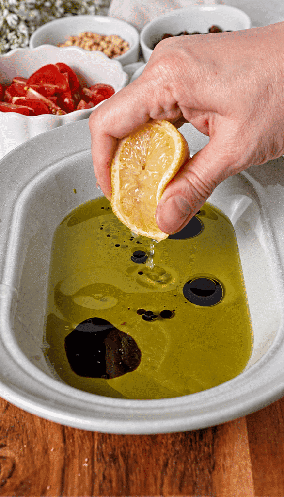 Fresh lemon squeezed into olive oil and balsamic vinegar in a serving bowl.