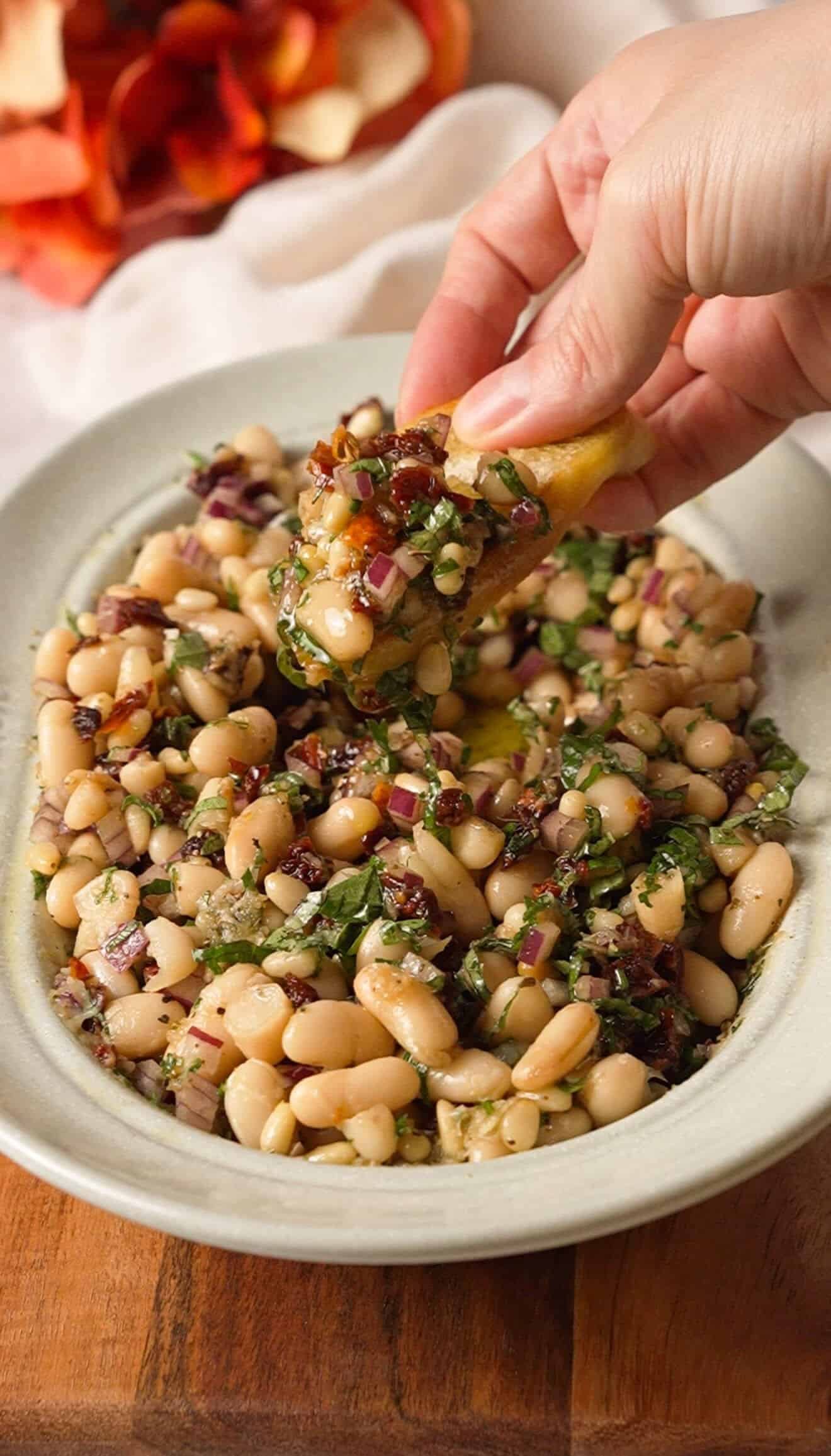 Dipping crusty bread into marinated white bean and sun-dried tomato dip
