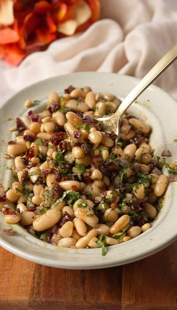 Spoon lifting a scoop of marinated white bean and sun-dried tomato dip