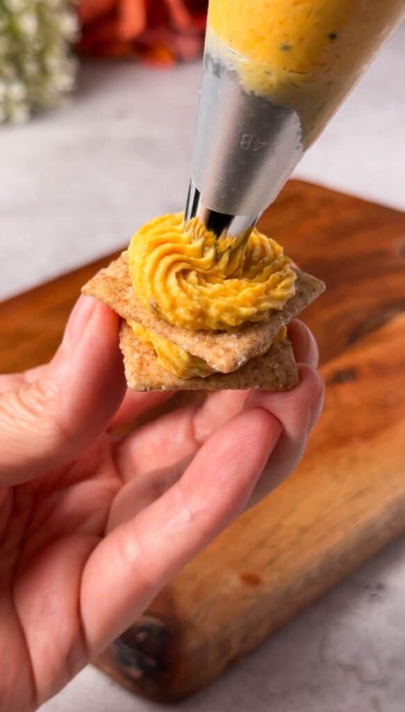 Piping butternut squash cheese onto stacked wheat crackers