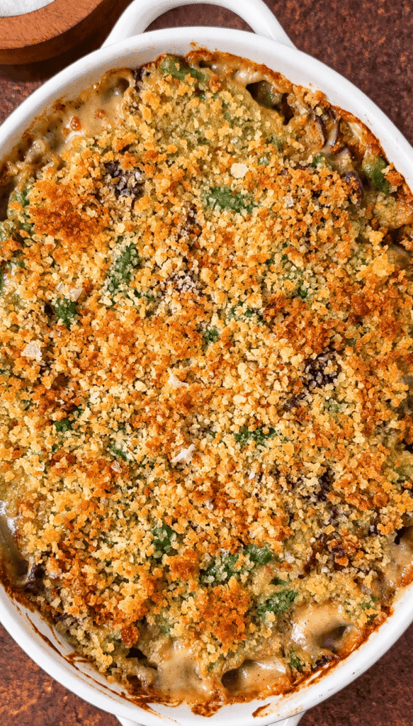 Baked green bean casserole with golden panko breadcrumbs and creamy mushroom sauce bubbling around the edges.