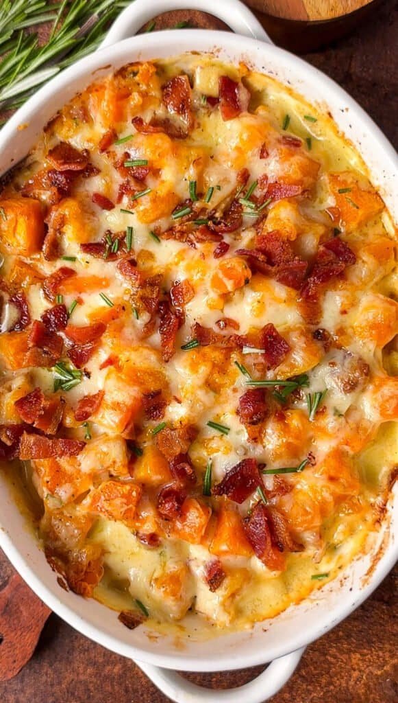 Baked butternut squash gratin with melted Gruyère, browned bacon, and rosemary in a white oval dish