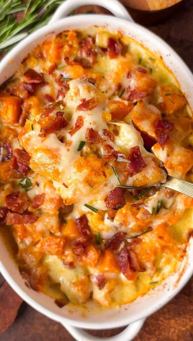 Spoonful of butternut squash gratin with melted Gruyère, bacon, and rosemary lifted above the baking dish