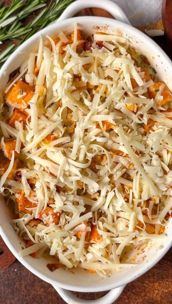 Assembled butternut squash gratin topped with grated Gruyère, ready for the oven